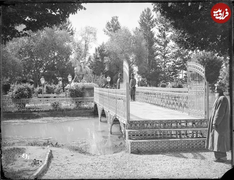 در اینجا تصویری از دوران قاجار را ملاحظه می‌کنید که مردانی با لباس مخصوص خدمت درباری را در محوطۀ باغشاه و در نزدیکی مجسمه ناصرالدین شاه نشان می‌دهد.